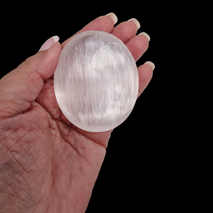 Selenite Palm Stone 70 mm shown on hand for scale black background