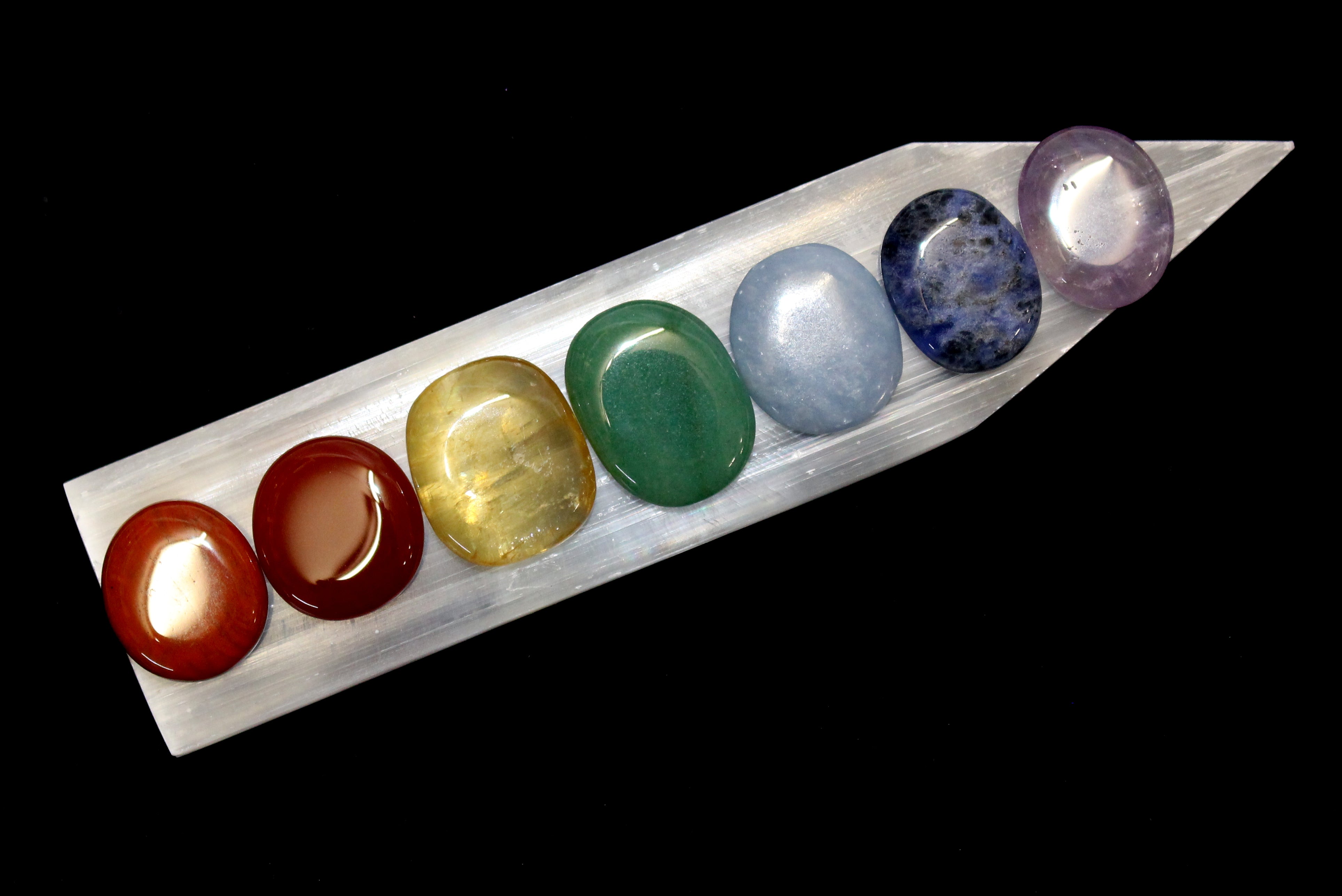 7 stones, red, orange, yellow, green, blue, purple on a charging white ruler, smooth stones polished