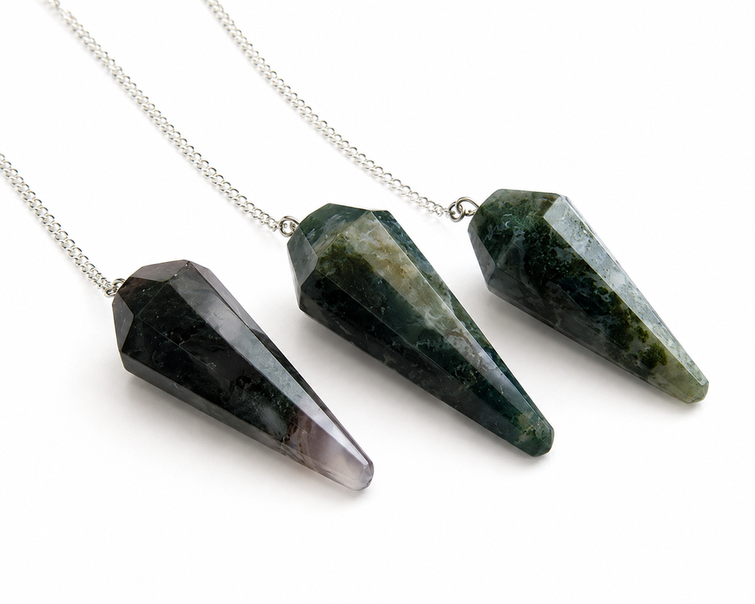Three faceted crystal cone pendants on silver chains, displayed diagonally on a clean white background. The crystals are dark green, black, and gray with natural stone textures.