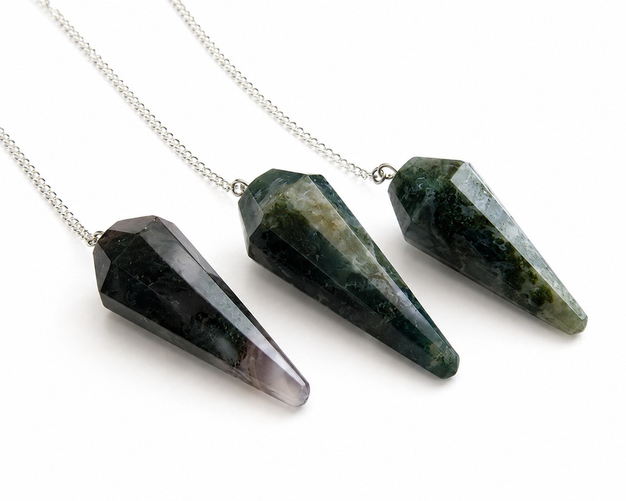 Three faceted crystal cone pendants on silver chains, displayed diagonally on a clean white background. The crystals are dark green, black, and gray with natural stone textures.