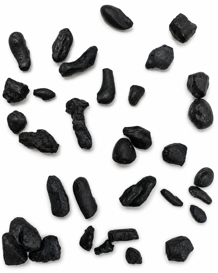 A collection of small, irregular black stones atacama Impact Glass pieces scattered on a plain white background.