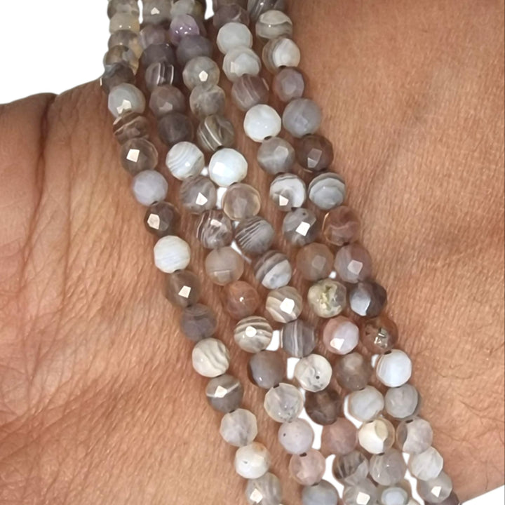 Botswana Agate 4mm faceted round beads held in a hand for scale