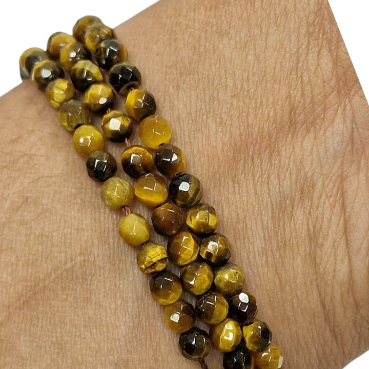 Gold Tigers Eye 4mm faceted round beads held in a hand for scale