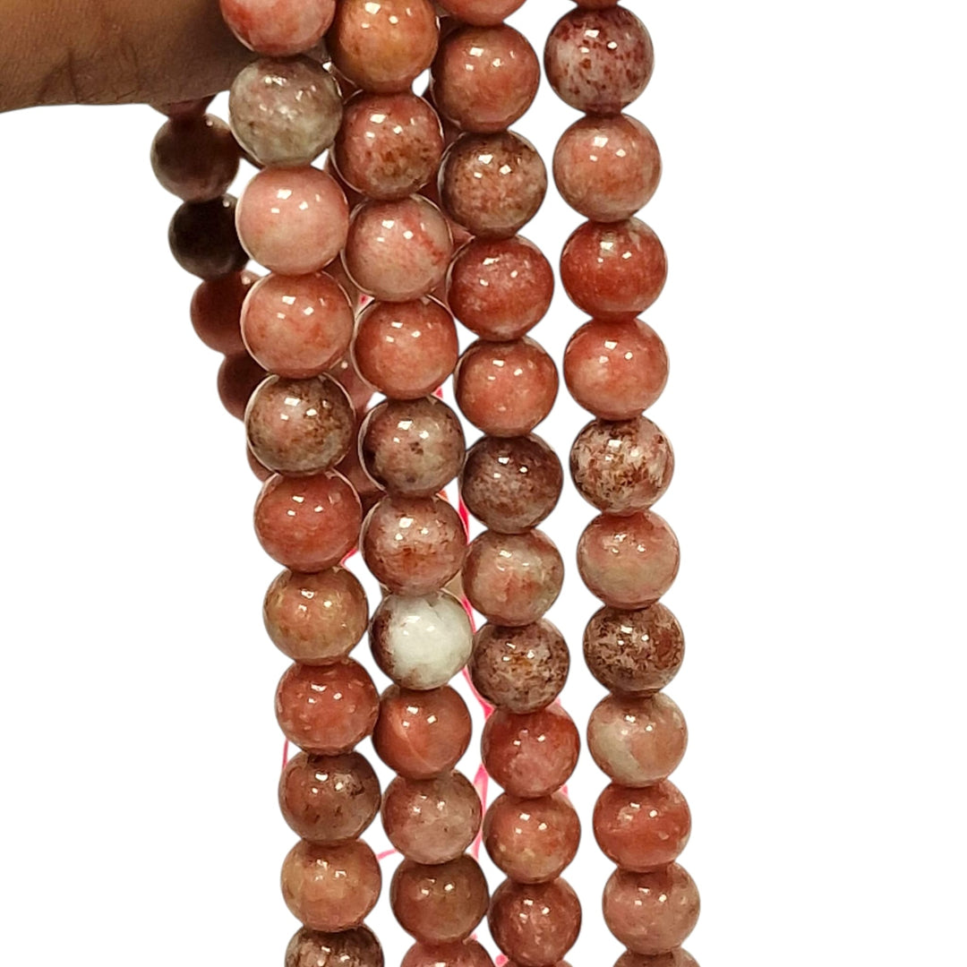 Pink Thulite round beads held in a hand for scale