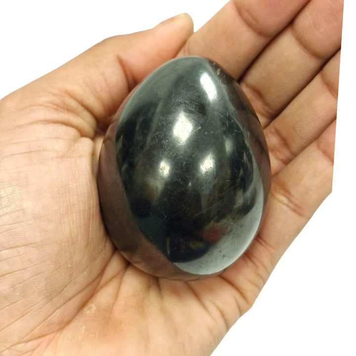 60mm polished Shungite egg on hand, grounding crystal for EMF protection and spiritual growth