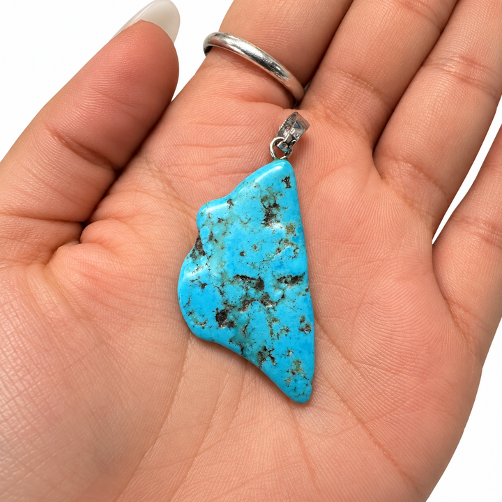 GeoFossils one-of-a-kind Kingman Mine Turquoise pendant displayed in the palm of a hand, showing its natural freeform shape, blue and dark matrix patterning and sterling silver fitting for scale.