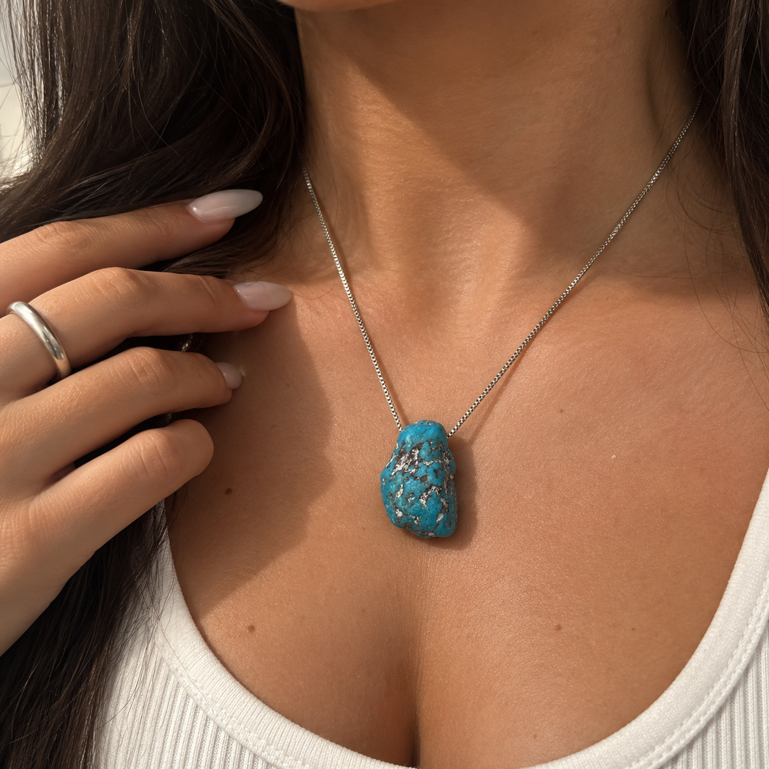 GeoFossils Kingman Mine Turquoise drilled tumblestone styled as a necklace on a model, suspended from a silver-coloured chain against a white top.