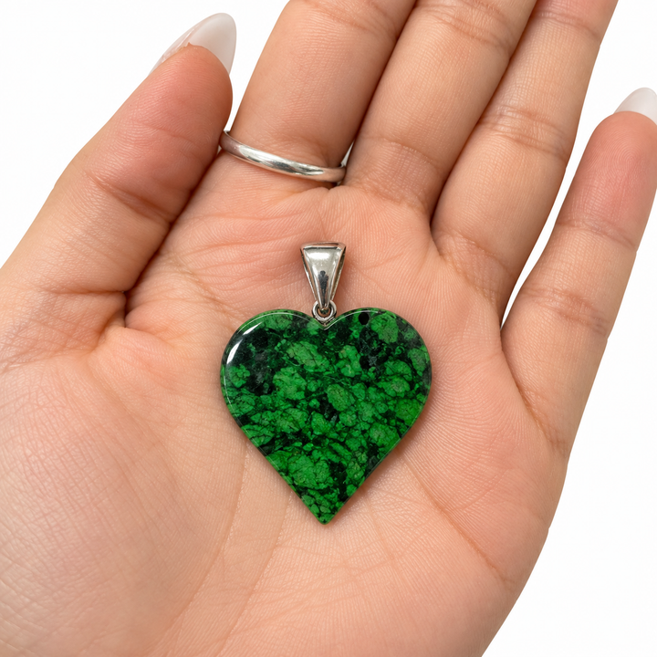 GeoFossils Maw Sit Sit heart pendant from Burma (Myanmar), featuring natural green and black patterning and a sterling silver bail, displayed in the palm of a hand to demonstrate its approximate 4 cm size and scale.