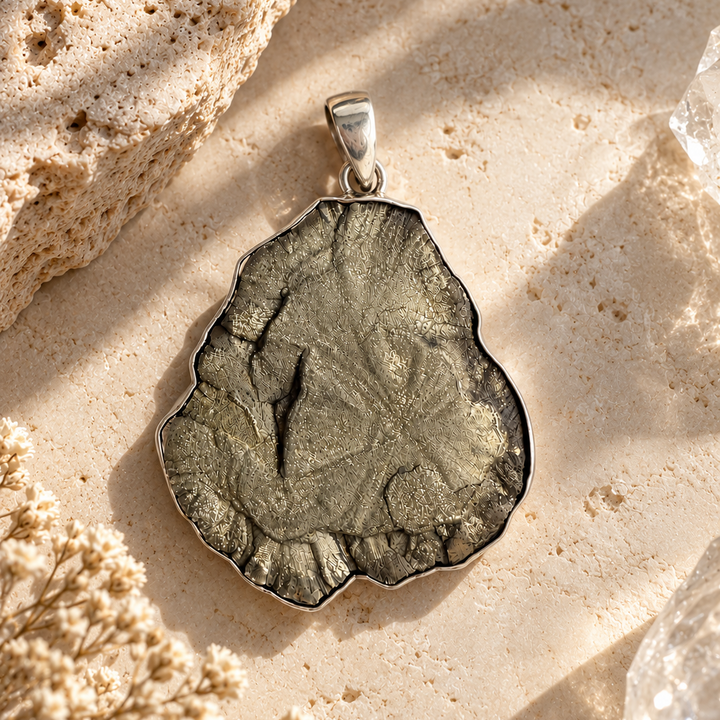Natural Pyrite Sun sterling silver pendant styled on a warm ivory stone surface with dried flowers and mineral accents.