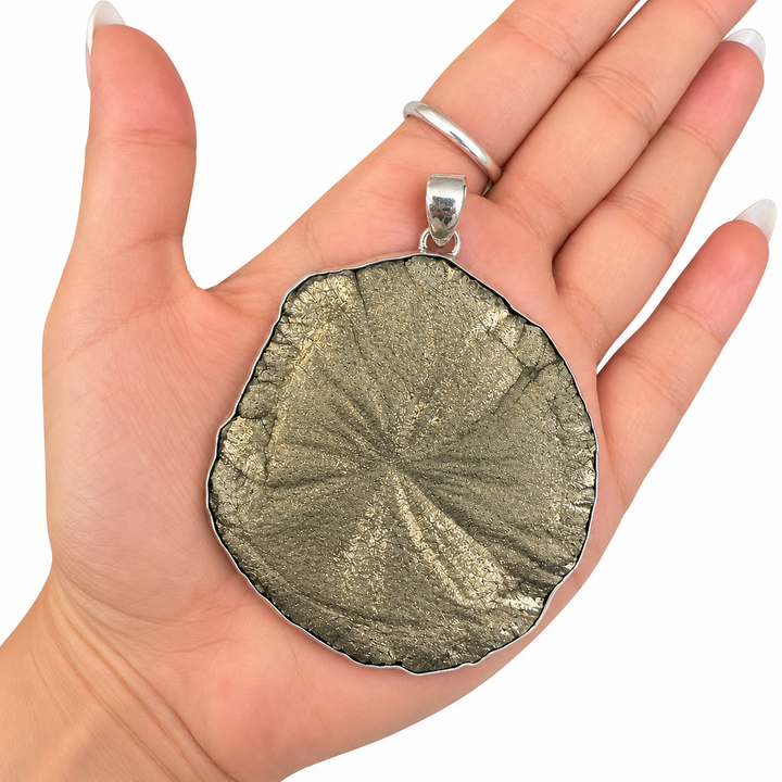 Large natural Pyrite Sun pendant resting in an open hand, showing its statement size, metallic golden-grey finish and silver bail