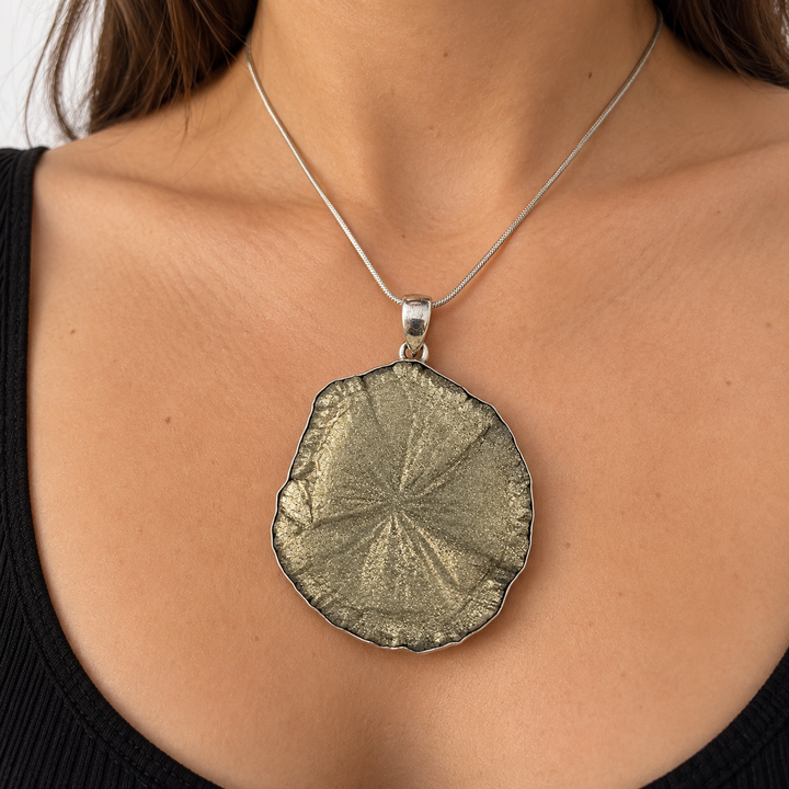 Statement Pyrite Sun pendant worn on a silver chain against a black top, showing the mineral's natural radial pattern and scale when worn.