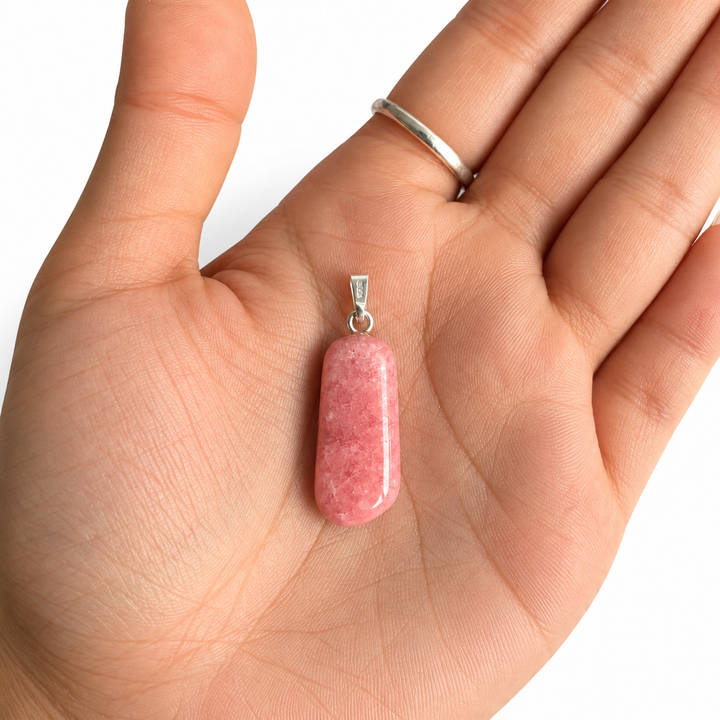 GeoFossils natural Rhodochrosite pendant resting in an open palm for scale, showing its polished pink gemstone, elongated shape and 925 sterling silver bail.