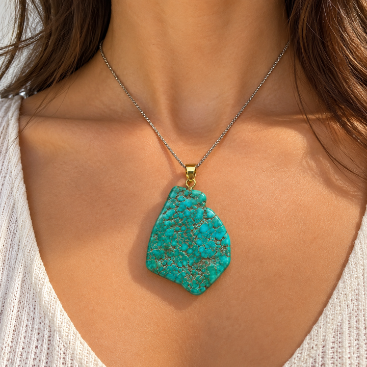 GeoFossils natural Royston Turquoise statement pendant styled on a model with a silver-coloured chain, featuring a polished blue-green gemstone and gold-tone bail.