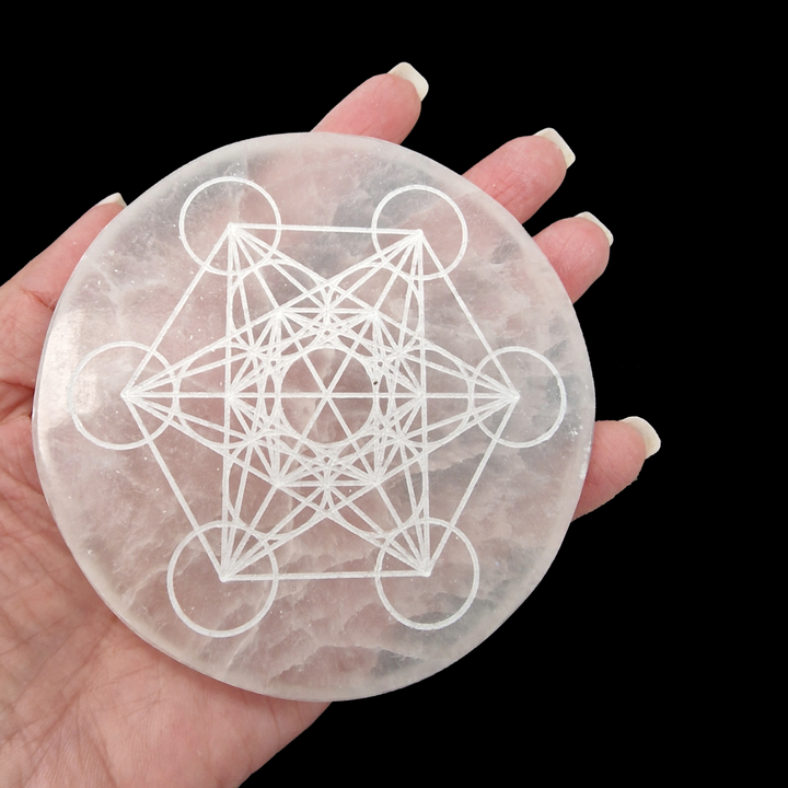 Selenite Charging Disc 10 cm engraved with Metatron’s Cube shown on hand for scale on black background