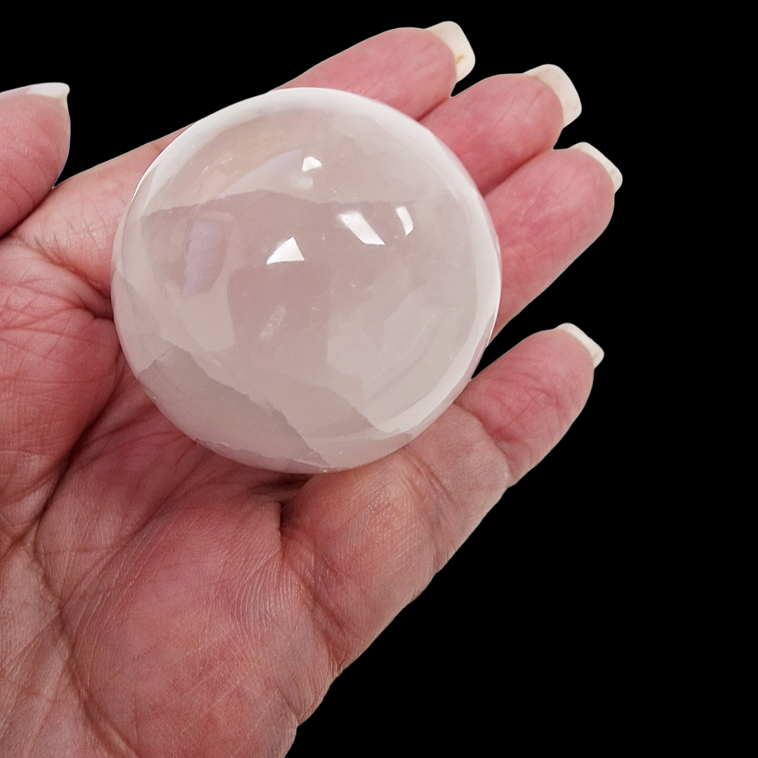 Selenite Sphere 40mm shown on hand for scale on black background