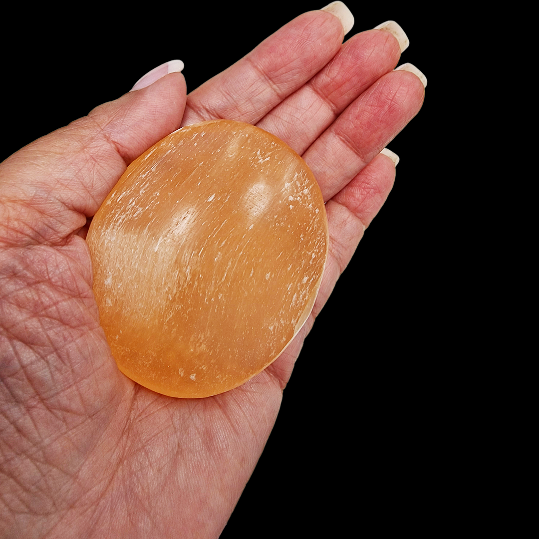 Peach Selenite Palm Stone 70 mm shown on hand for scale on black background