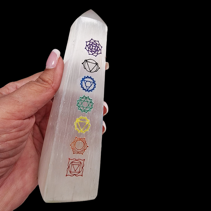 Selenite Chakra Tower 12cm polished with 7 chakra symbols, shown in hand for scale. Black Background.