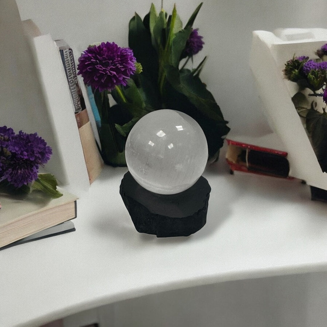 Decorative setup with Selenite sphere on a shungite base, surrounded by books and flowers for energy cleansing.