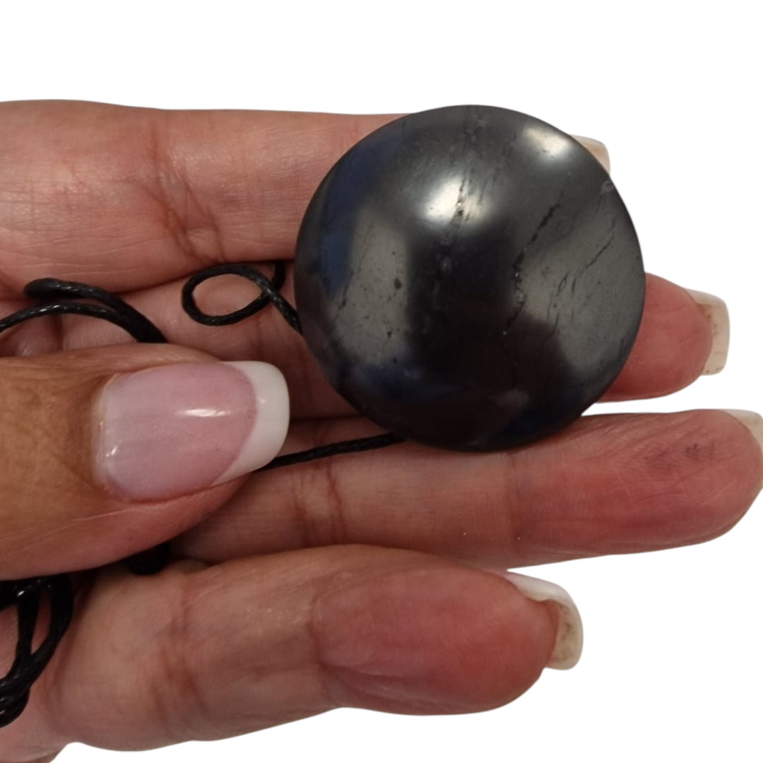 Yo-Yo style Shungite pendant with black cotton cord on hand, vegan-safe EMF protection necklace