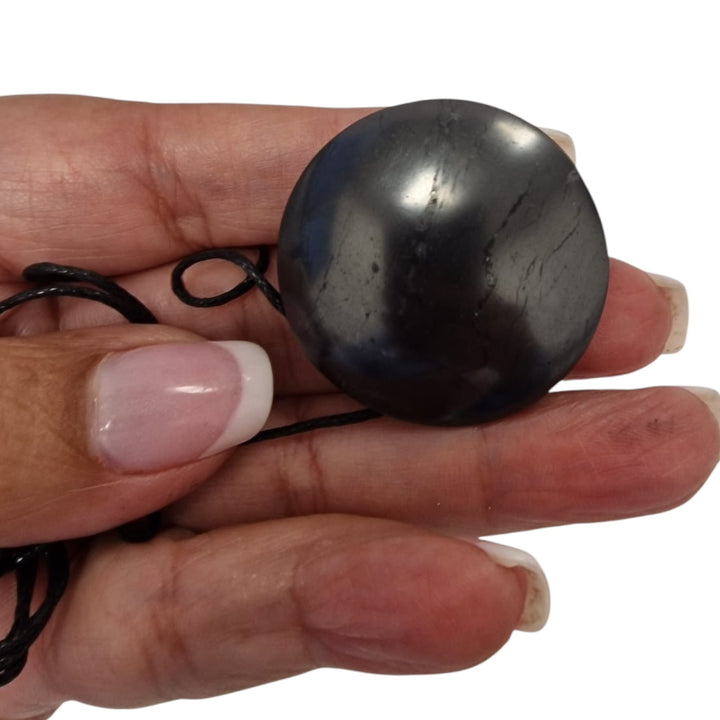 Yo-Yo style Shungite pendant with black cotton cord on hand, vegan-safe EMF protection necklace