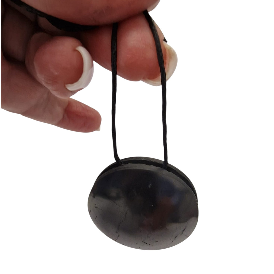 Yo-Yo style Shungite pendant with black cotton cord on hand, vegan-safe EMF protection necklace