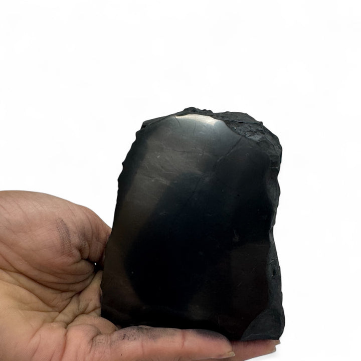 Hand holding a medium one-face polished shungite crystal, showing its glossy surface and raw black edges.