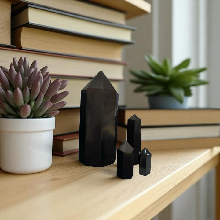 Group of polished shungite towers in 5cm, 10cm, and 20cm sizes on a wooden shelf with books and succulents, perfect for meditation or decor.