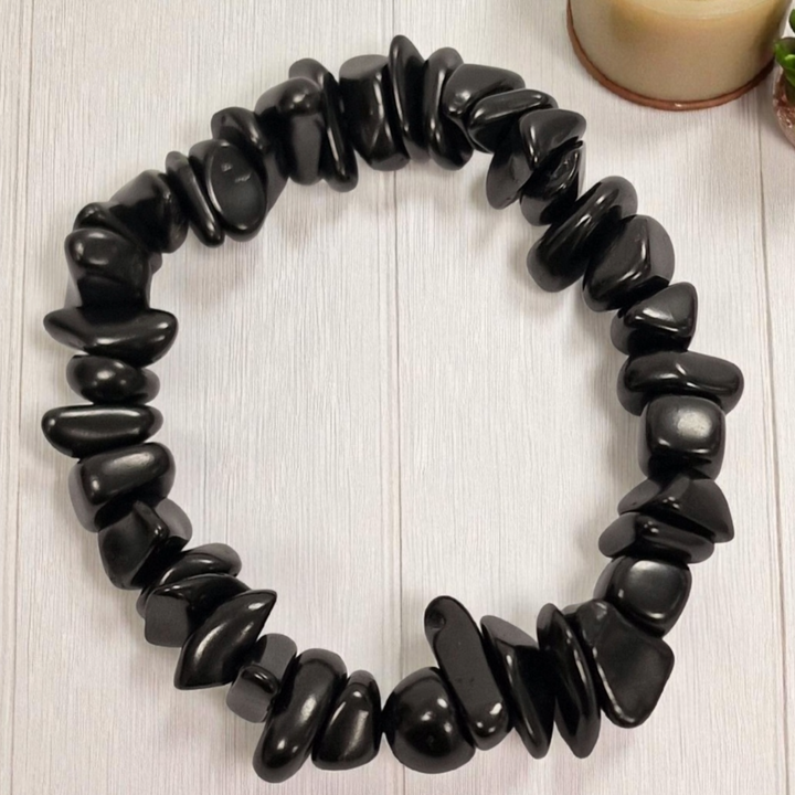 Close-up of Shungite gem chip bracelet on white wooden background, grounding and cleansing crystal bracelet