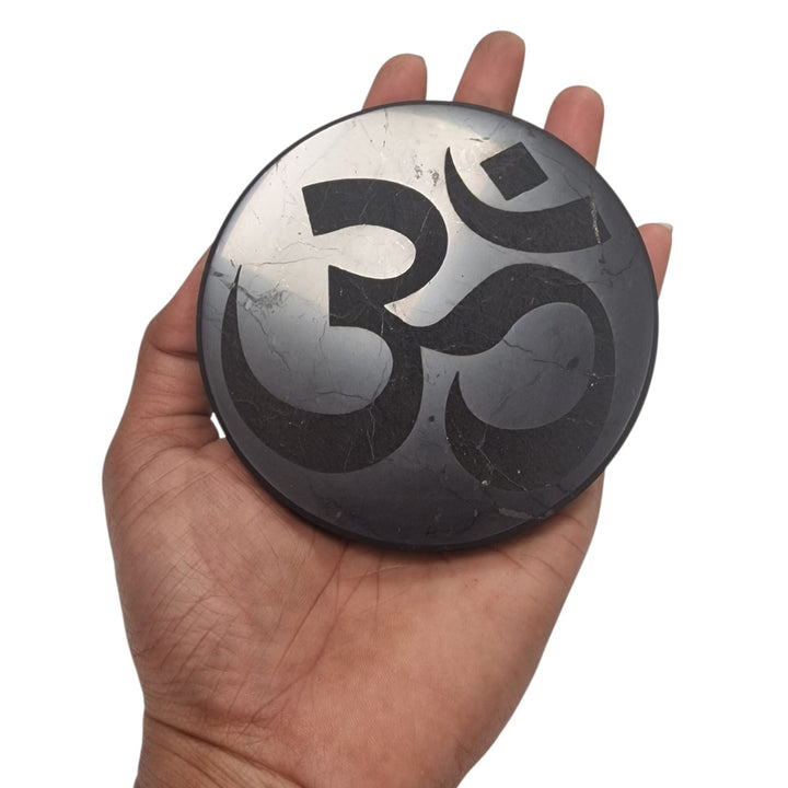Shungite 10cm round Ohm charging disc on hand for size reference, grounding and EMF protection crystal