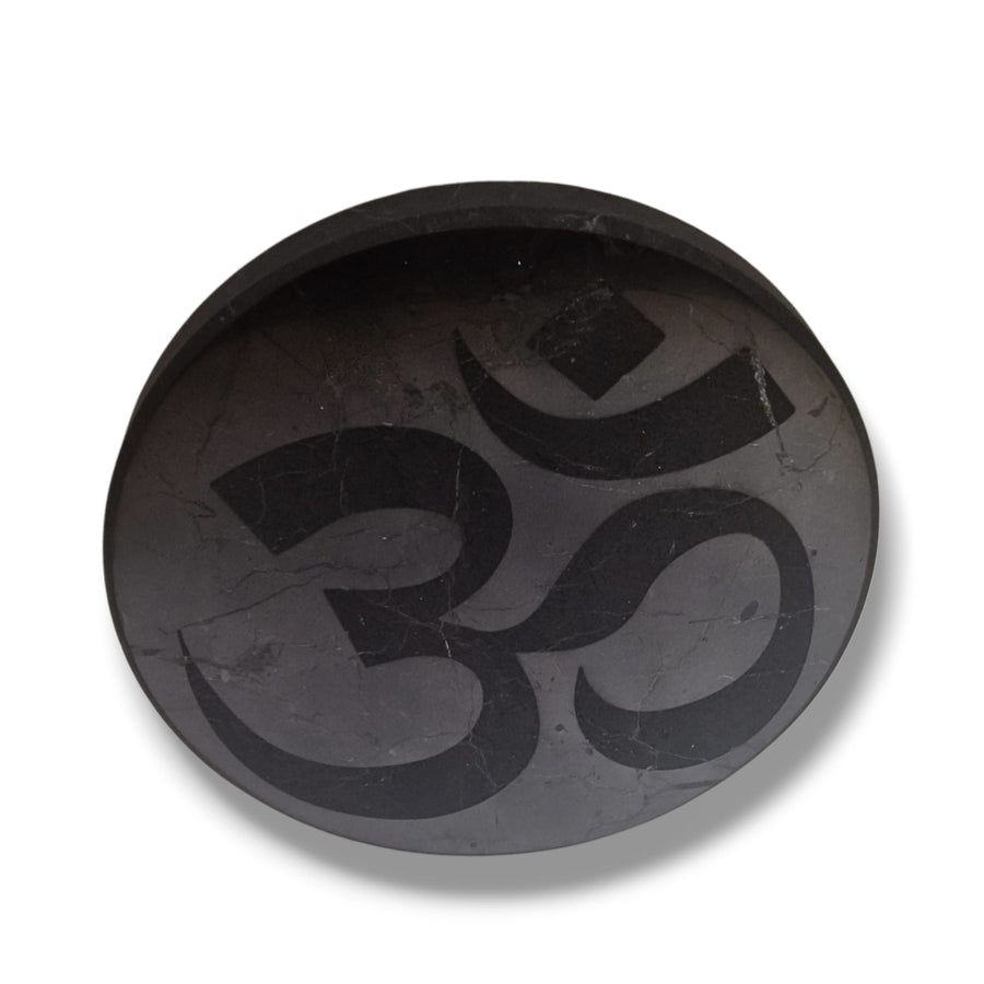 Shungite 10cm round disc with engraved Ohm symbol on white background, charging plate for crystals and meditation