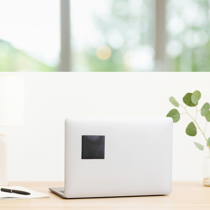 Shungite protective square slice applied to back of laptop lid in clean home office environment