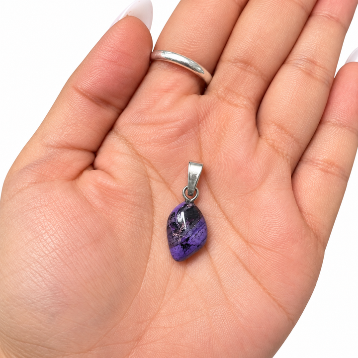 GeoFossils Sugilite pendant resting in an open palm to demonstrate its petite proportions, featuring a polished purple gemstone and sterling silver bail.