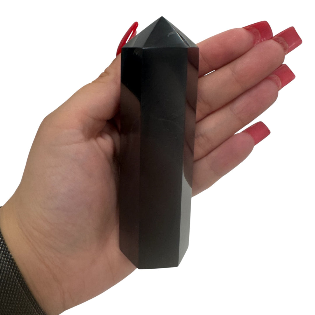 Hand holding a 10cm polished shungite tower point, showing size and glossy black finish