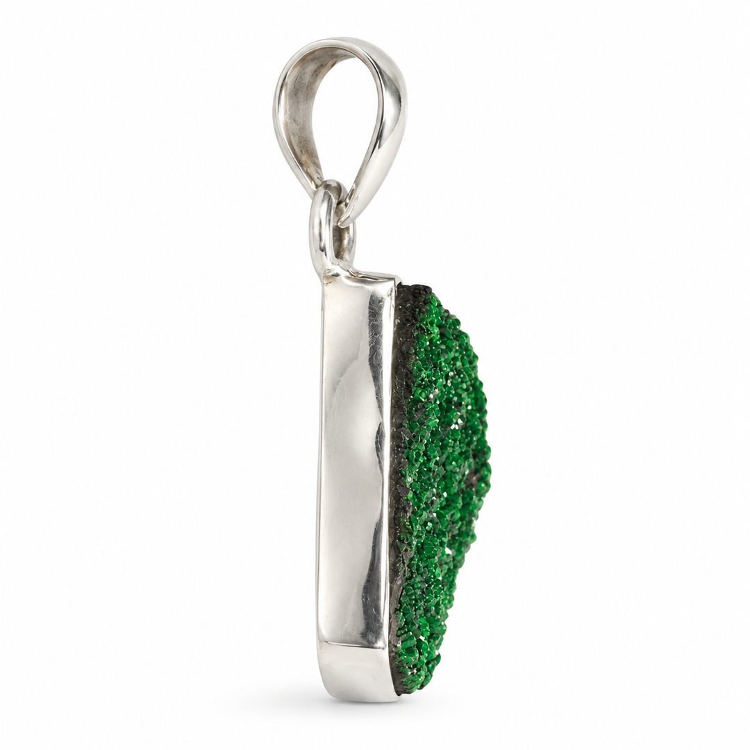 GeoFossils natural Uvarovite Garnet pendant in side profile, displaying its raised green crystal surface, dark matrix edge and polished silver setting.