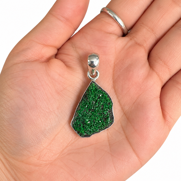 GeoFossils natural Uvarovite Garnet pendant resting in an open palm against a white background, showing the gemstone's size, green druzy crystals and silver bail.