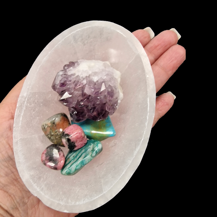 Hand holding a selenite dish with various crystals on a black background