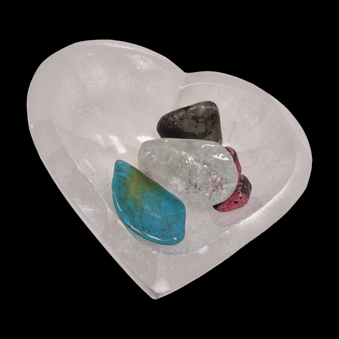 Back of Selenite Charging Bowl 8 cm heart shape with crystals, tumblestones on a black background.