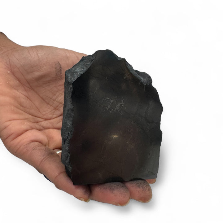 Hand holding a one-face polished shungite stone, highlighting its smooth surface and rough natural edges.