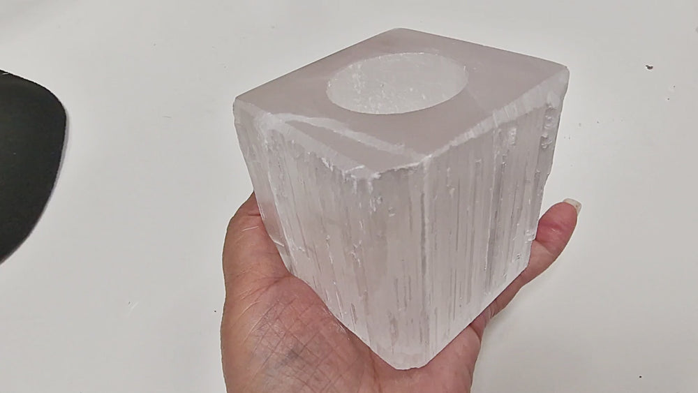 18-second video of a Selenite Square Tea Light Holder with polished top and base, raw sides. The holder is rotated in hand to show the polished surfaces and raw natural edges, with a tea light placed to demonstrate glow. Candle not included.