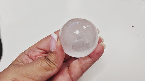 14-second video of a Selenite Sphere 40mm being rotated in hand, showing its smooth polished surface, luminous glow, and natural striations from every angle. Sphere stand used for demonstration but not included.