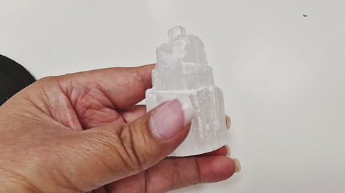 13-second video of a Selenite Tower 5cm in raw iceberg mountain effect style, rotated in hand to display its rugged sides, stepped layers, and glowing natural finish from all angles.