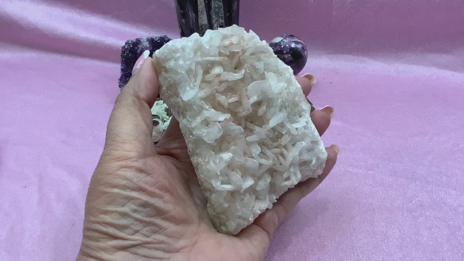 A gentle pan across the Blush Pink Celestite specimen, highlighting its soft pink crystals sparkling under natural light, showcasing its rare colour and delicate structure.