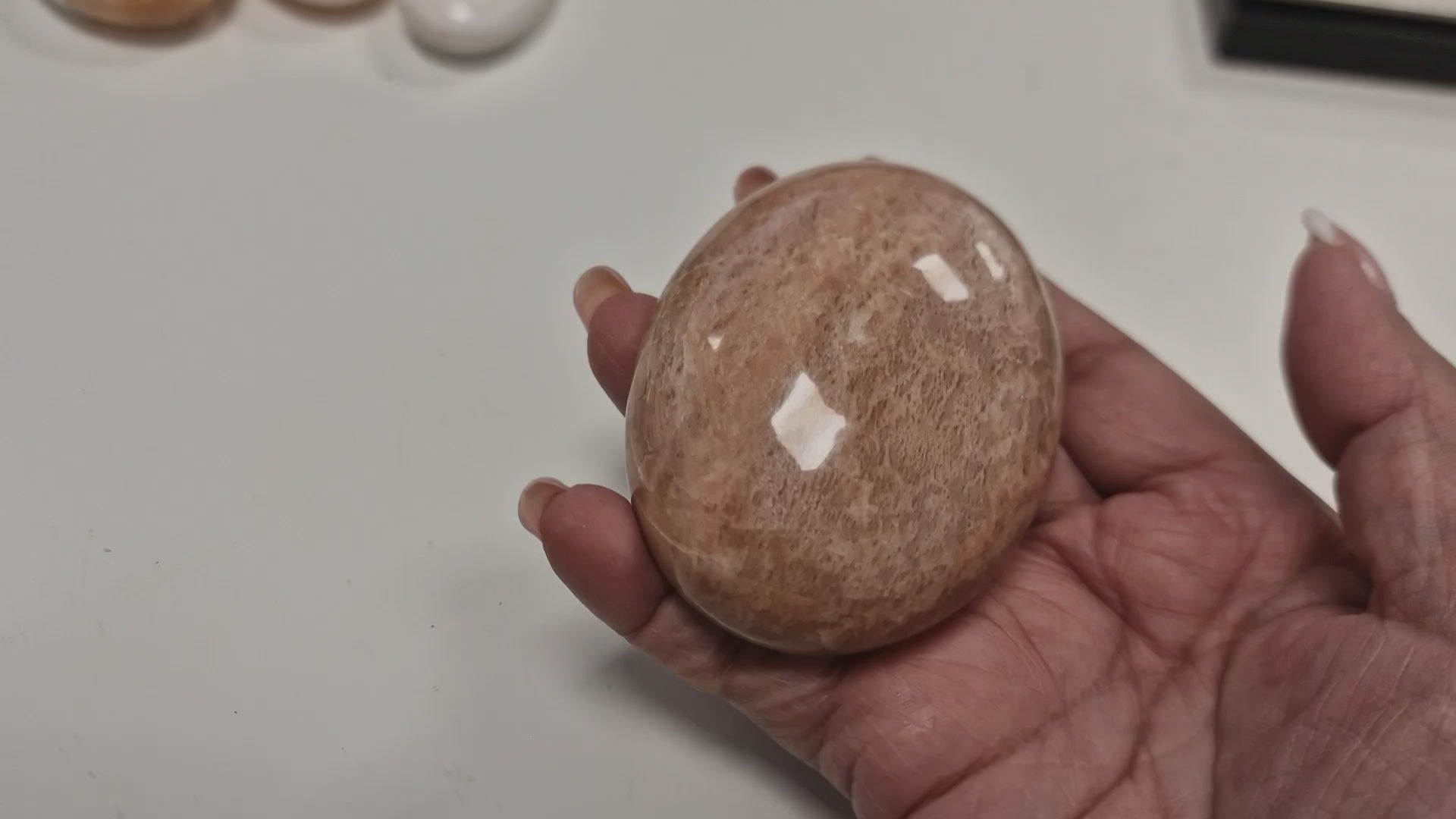 Slow rotation of the Peach Moonstone palm stone under natural light, highlighting its silky shimmer and warm, nurturing hue.