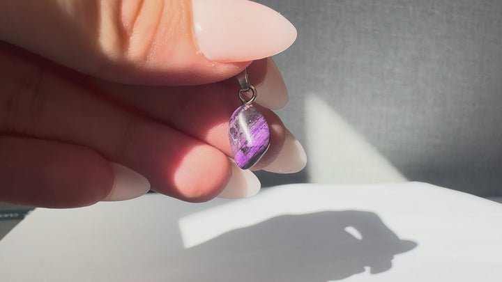 GeoFossils natural Sugilite pendant weighing 1.3g, shown from multiple angles to highlight its deep purple colouring, natural dark veining, polished freeform shape and sterling silver bail.